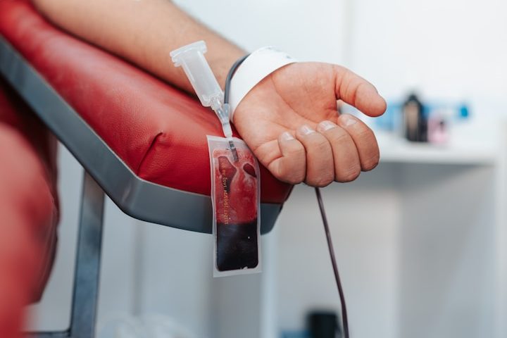 A healthcare professional holding a blood sample tube near a patient’s arm.